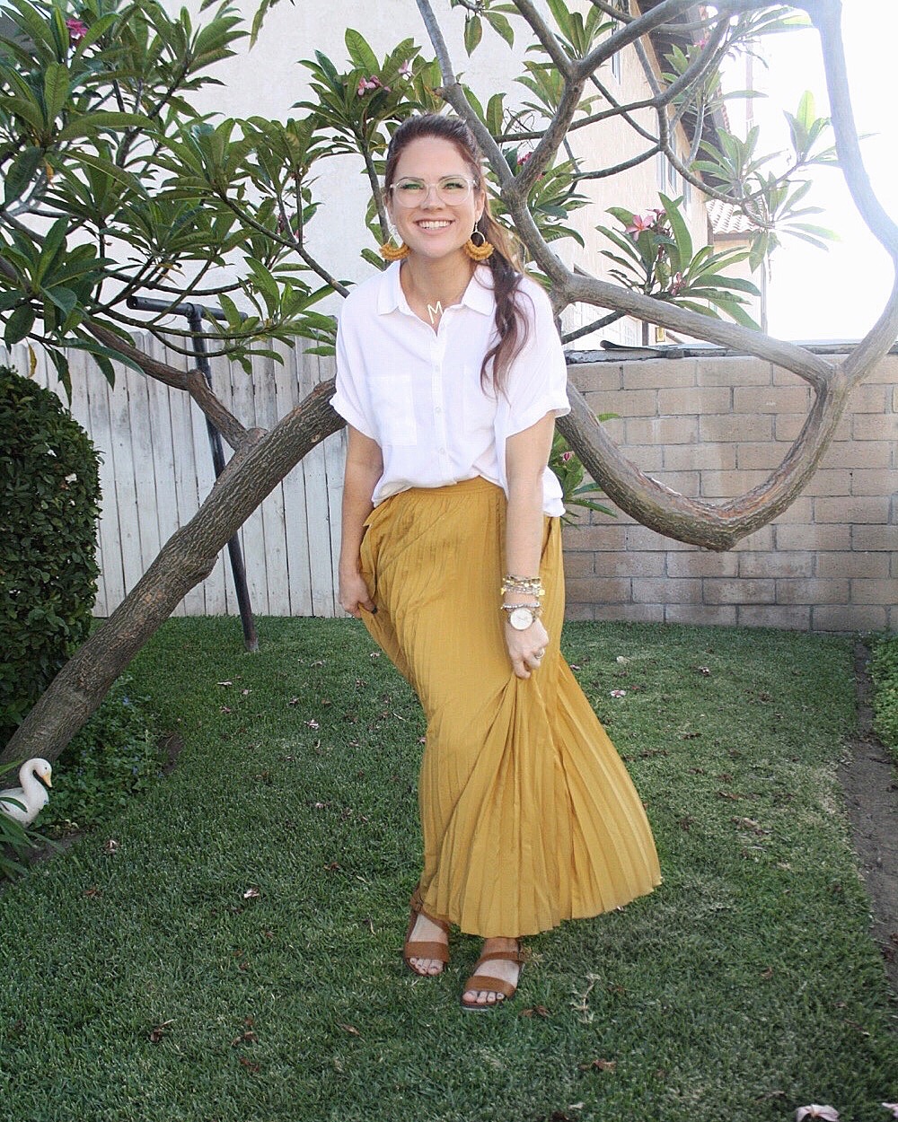 Katie Dunlavy, Lularoe boutique owner, of The Pearl Pages standing outside smiling in the grass by a tree in a long yellow skirt and white shirt.